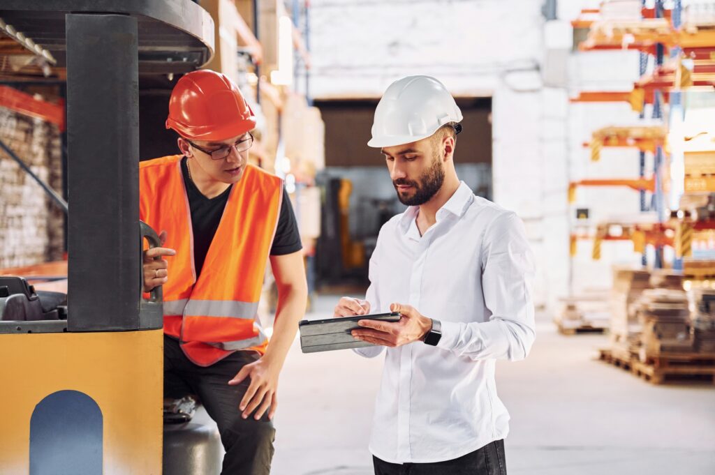 With tablet and cargo moving transport. Two storage workers is in the warehouse